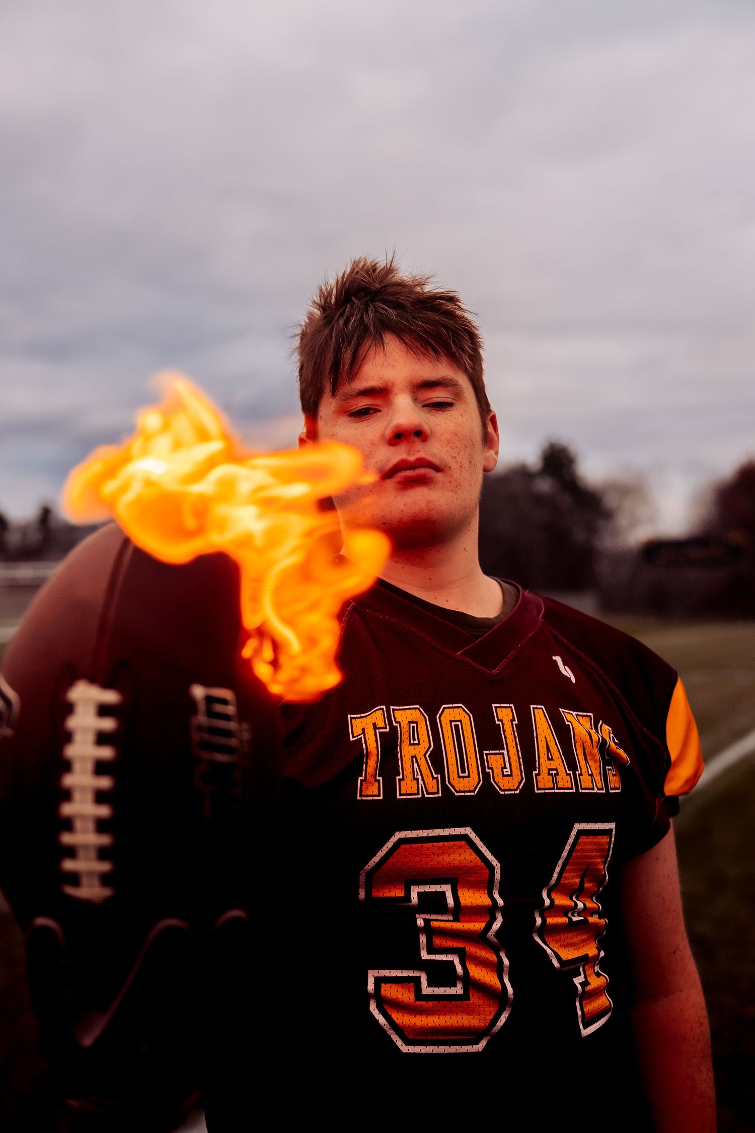 Trojans football player #34 holding a flaming ball on a field, wearing a dark jersey with dramatic fire effect.