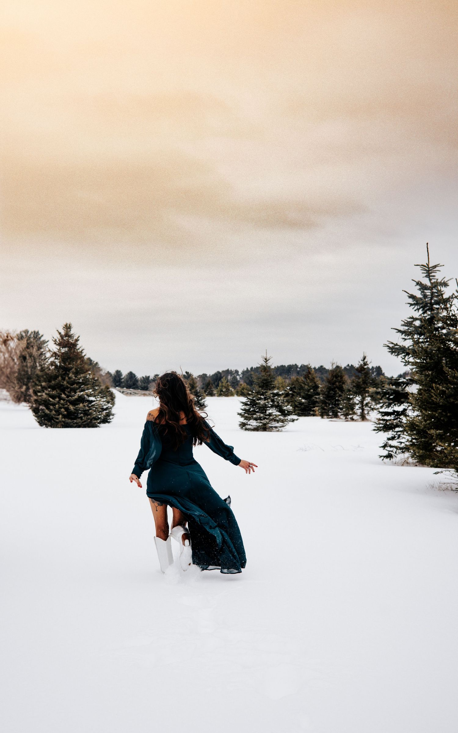 Person in dark coat walking through deep snow in a peaceful winter landscape with evergreen trees.
