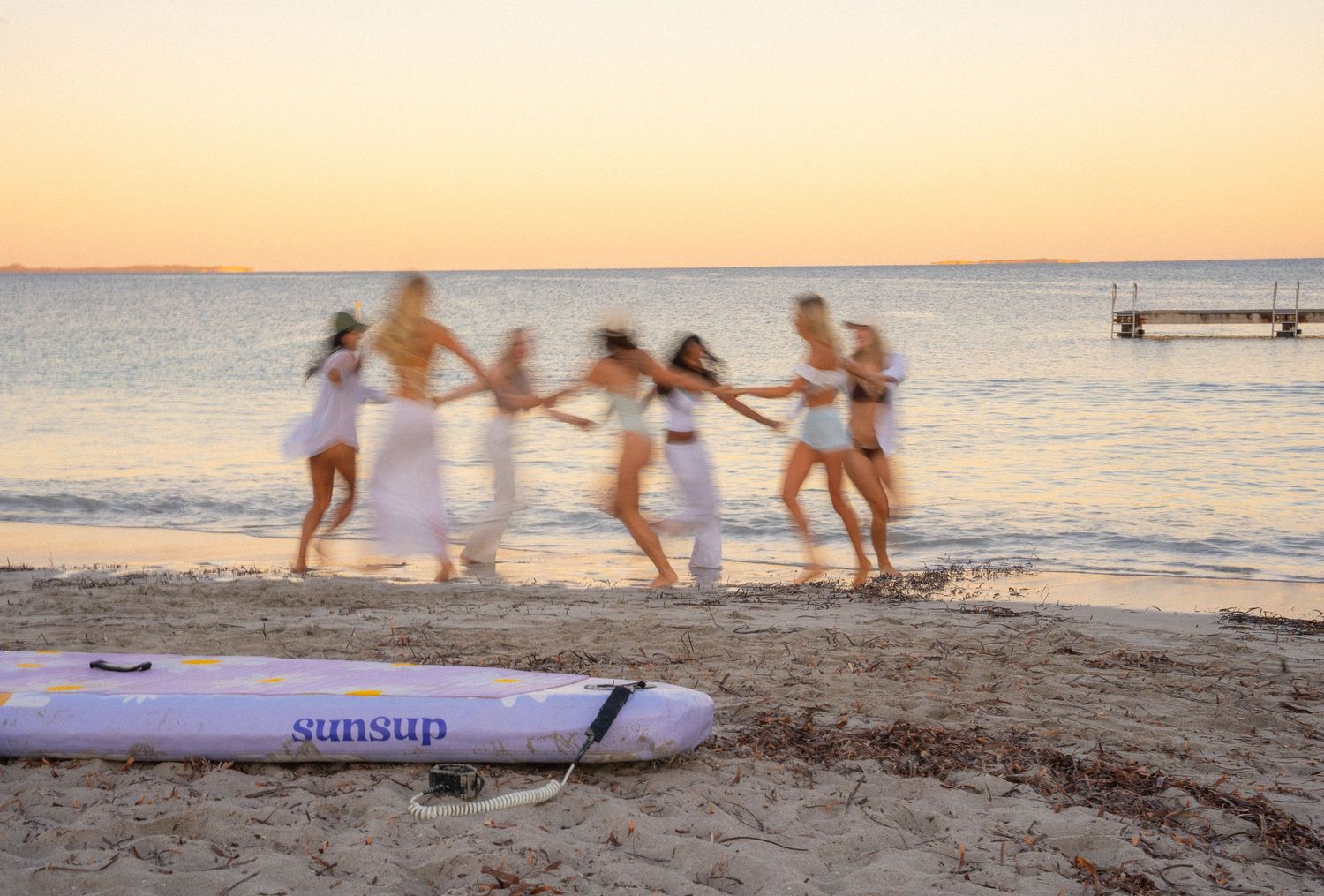 A group walks along a boat deck wearing beachwear and coverups during a sunset cruise on the ocean.