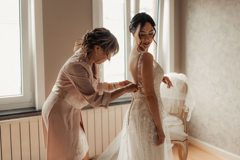 Ethereal wedding preparation scene with soft natural light streaming through windows as bride gets dressed.