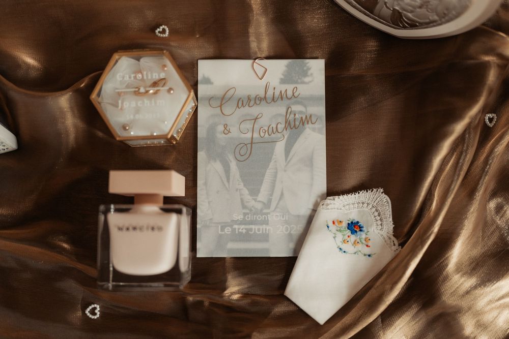 Wedding invitation suite with perfume bottle and decorative elements arranged on brown silk fabric.