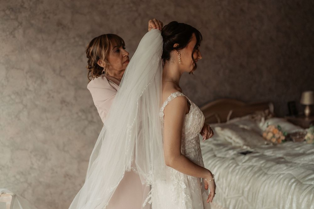 A bride in a wedding dress embraces someone during an emotional moment in a rustic setting.