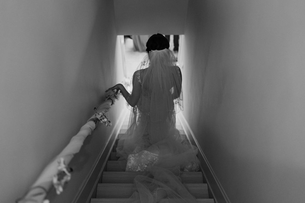 Black and white view of a shadowy figure ascending stairs in a narrow hallway creating an eerie atmosphere.