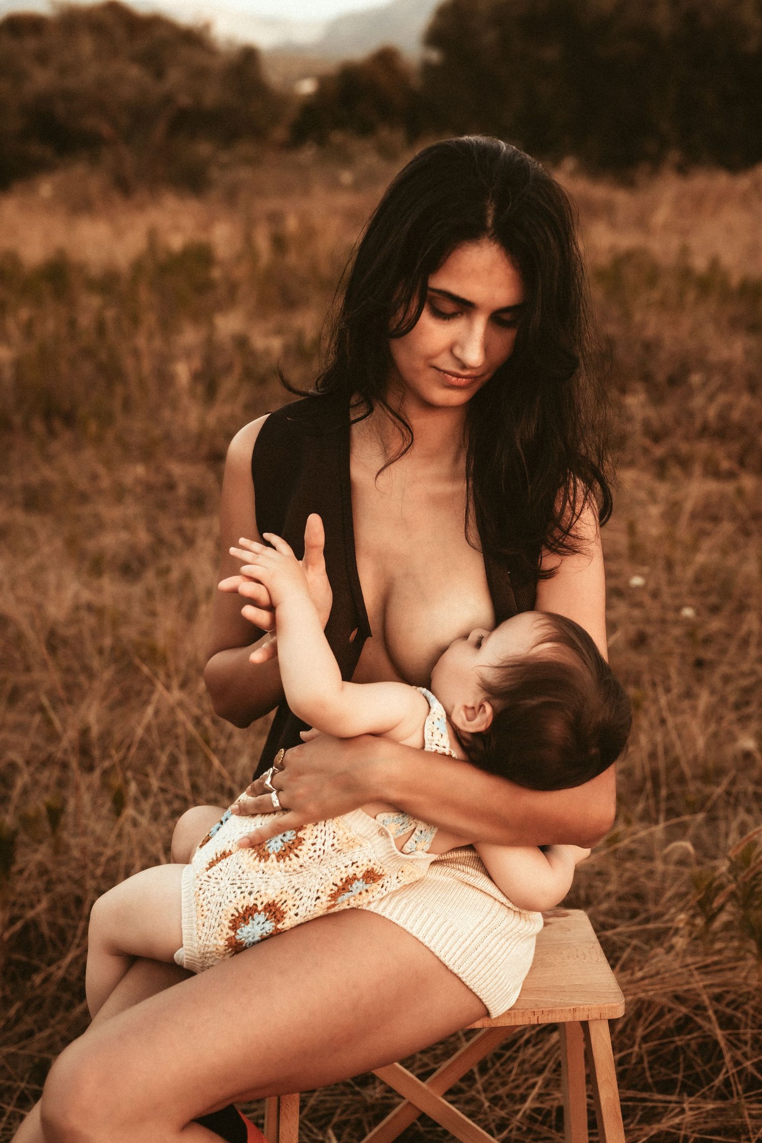 A parent tenderly nurtures an infant while sitting on a wooden stool in a rustic outdoor setting at sunset in Javea. Javea photographer