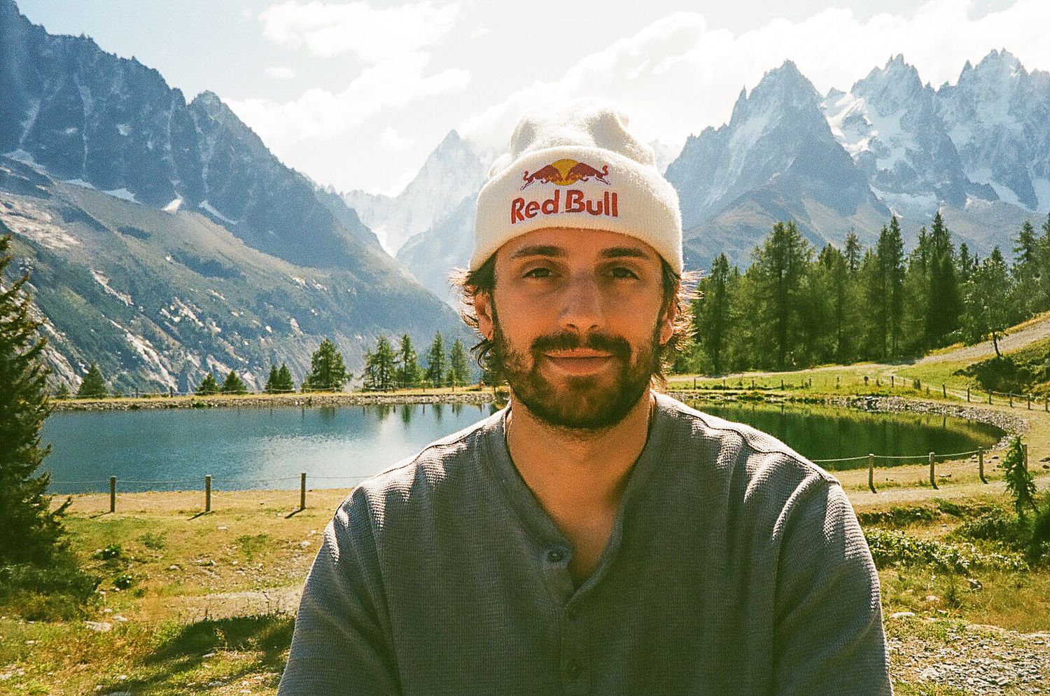 Mountain landscape with lake and peaks behind person wearing Red Bull cap.