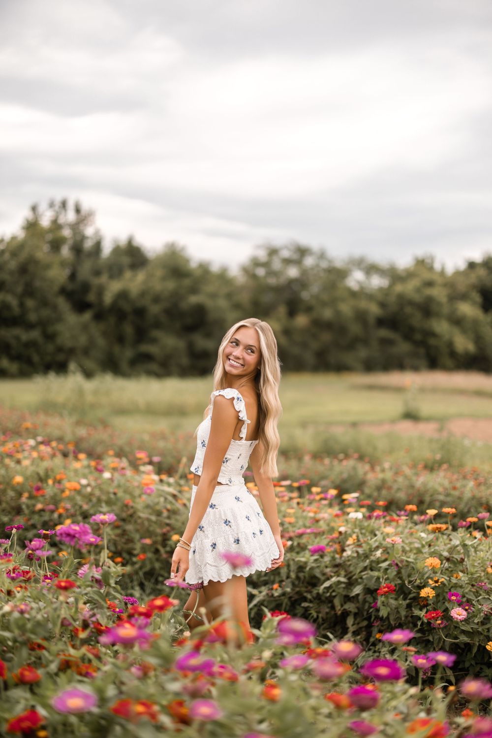 A figure in a white floral dress poses joyfully in a vibrant wildflower field during golden hour.