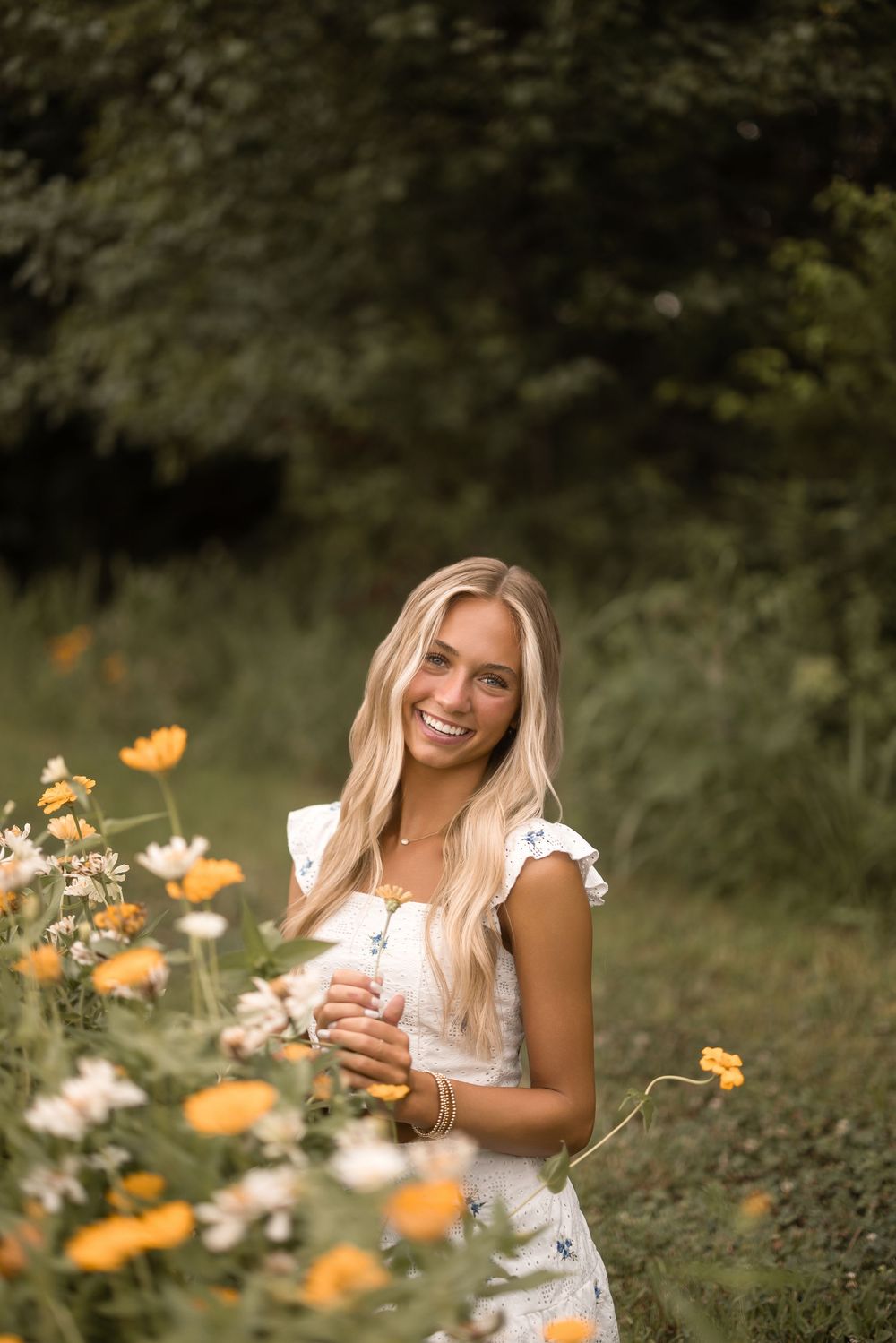 A figure stands among yellow and white wildflowers wearing a light summer dress on a sunny day.