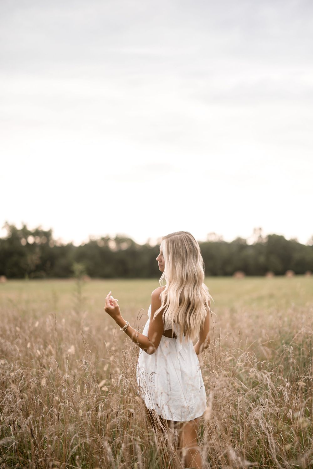 Woman wearing white summer dress stands in golden field at sunset with flowing hair and dreamy atmosphere.