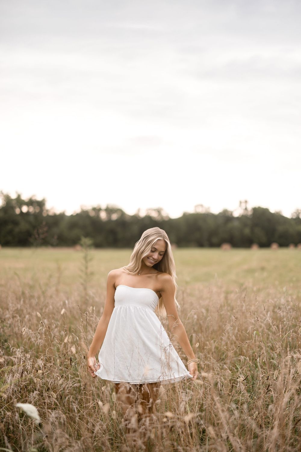 Young woman in a white sundress stands in a golden field at sunset.