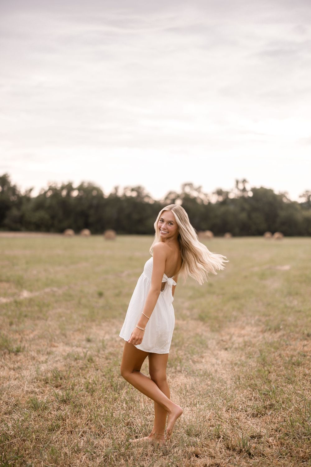 Figure in flowing white dress twirls joyfully barefoot in a sunlit meadow.