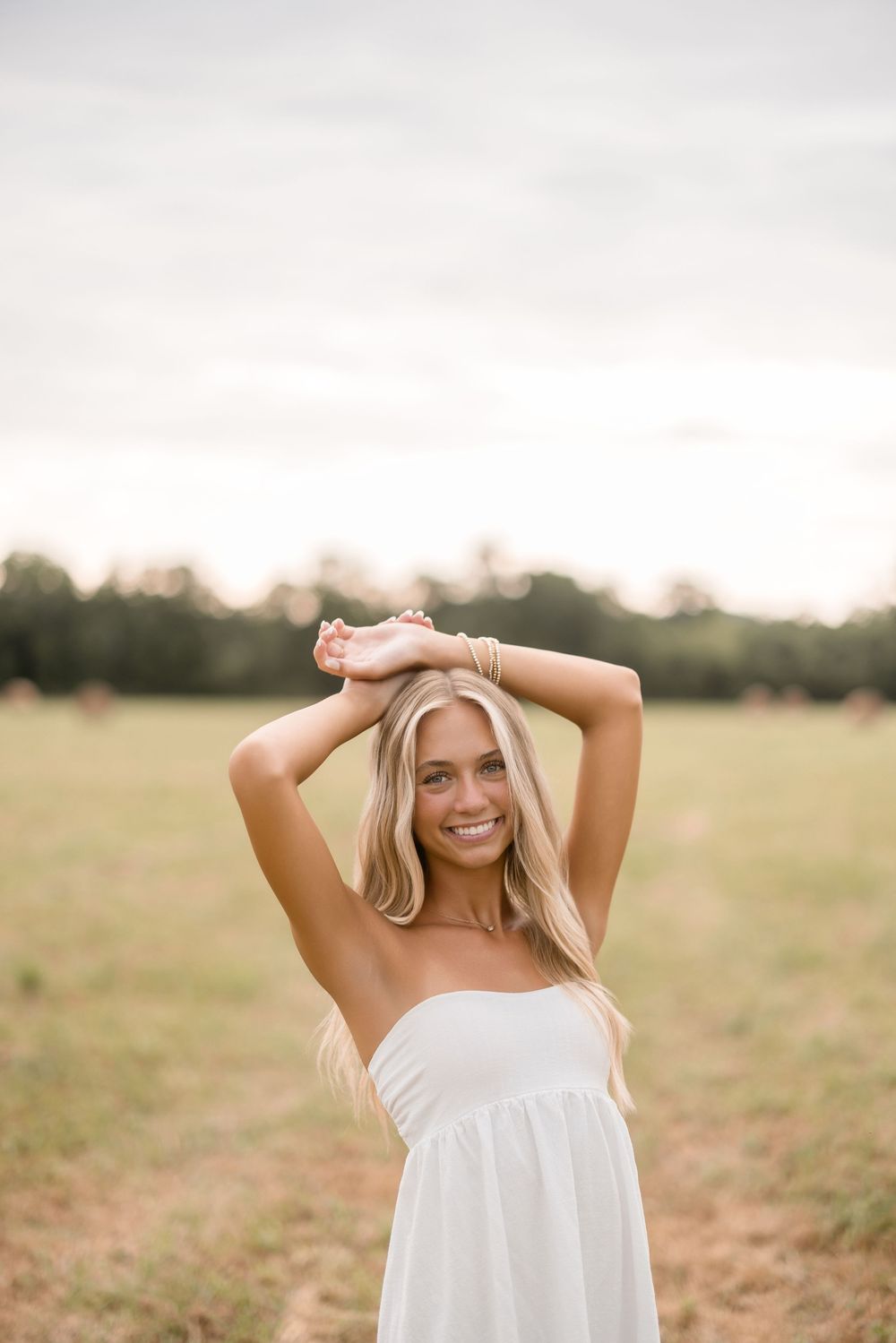 A summertime portrait in a field wearing a white dress against a golden sunset background.
