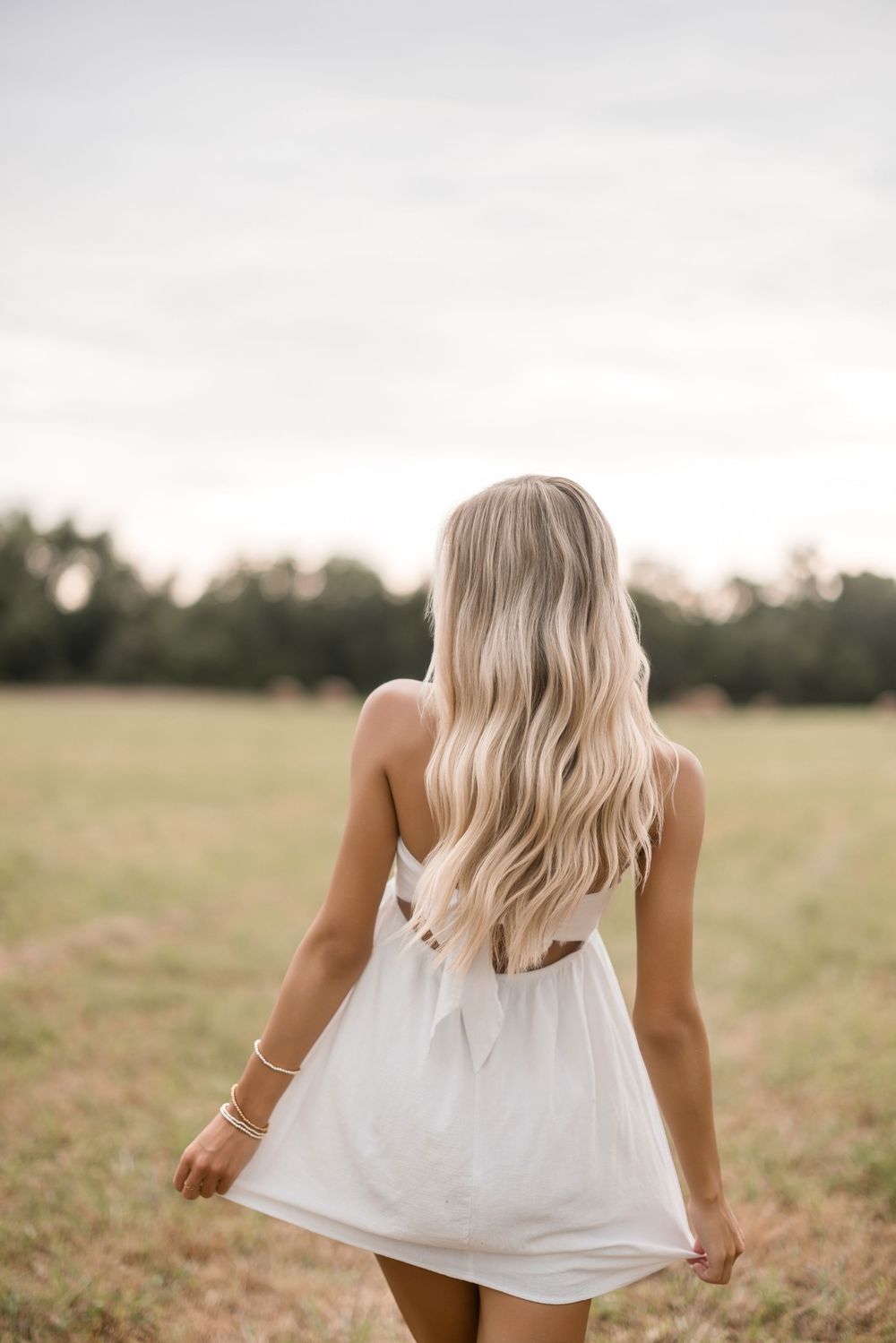 White flowy top twirling in a sunlit meadow against a soft cloudy sky.