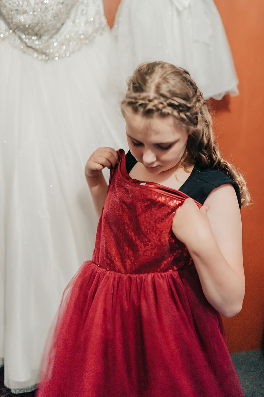 Elegant braided hairstyle and deep red velvet dress with tulle skirt shown against white gown backdrop.