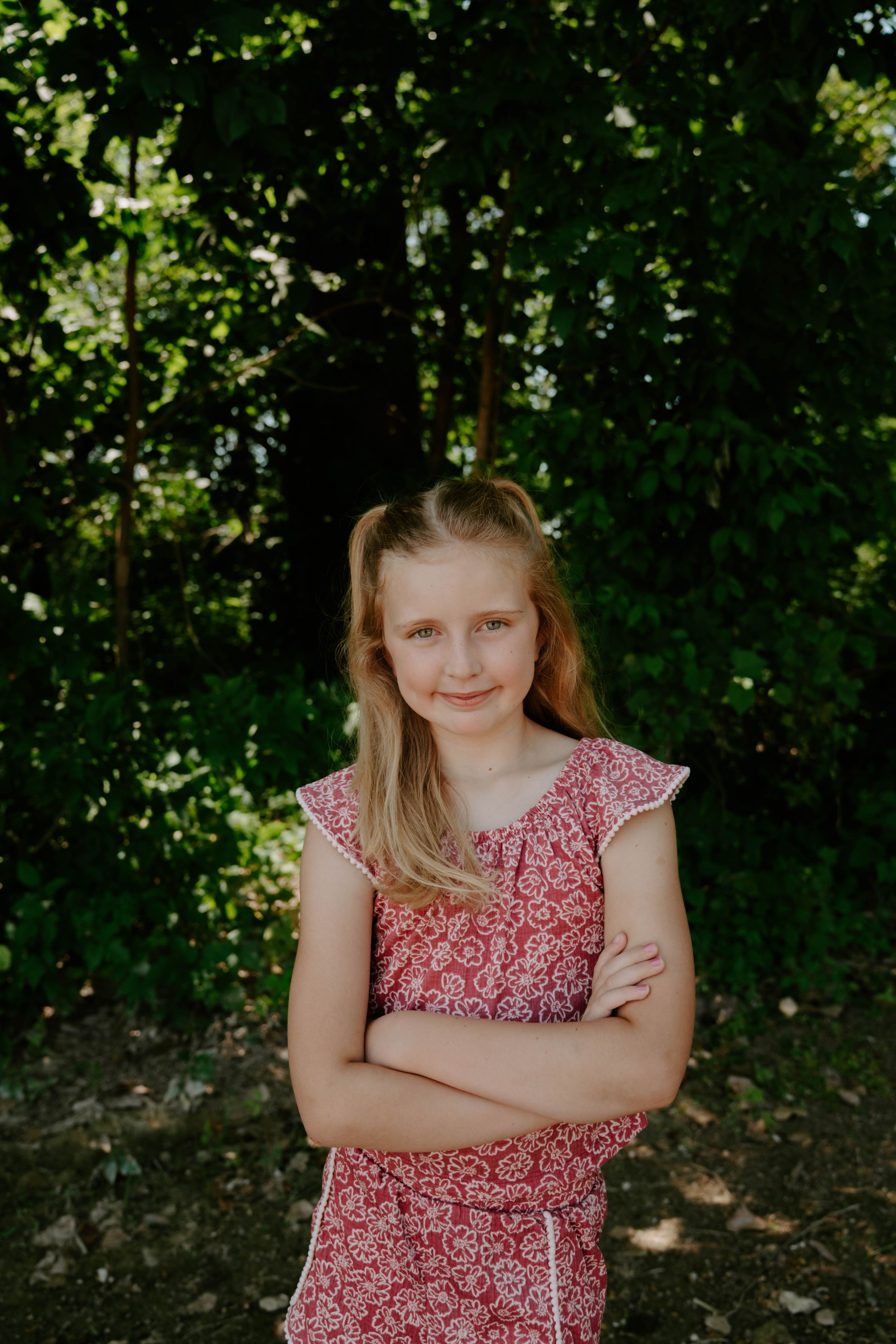 Two siblings wearing floral dresses smile while standing in a wooded outdoor setting.