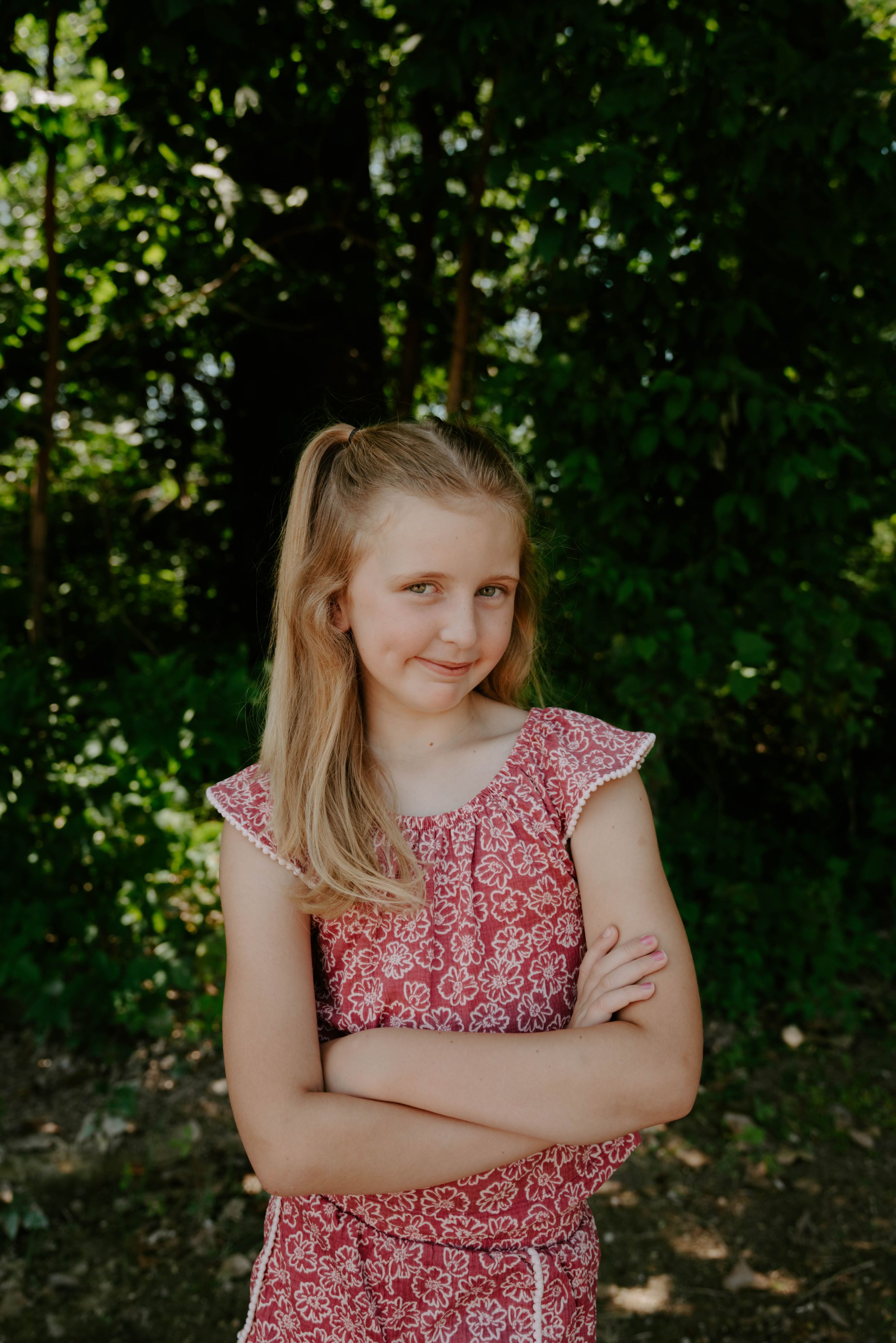 Two children in floral dresses pose against a leafy green background in natural lighting.