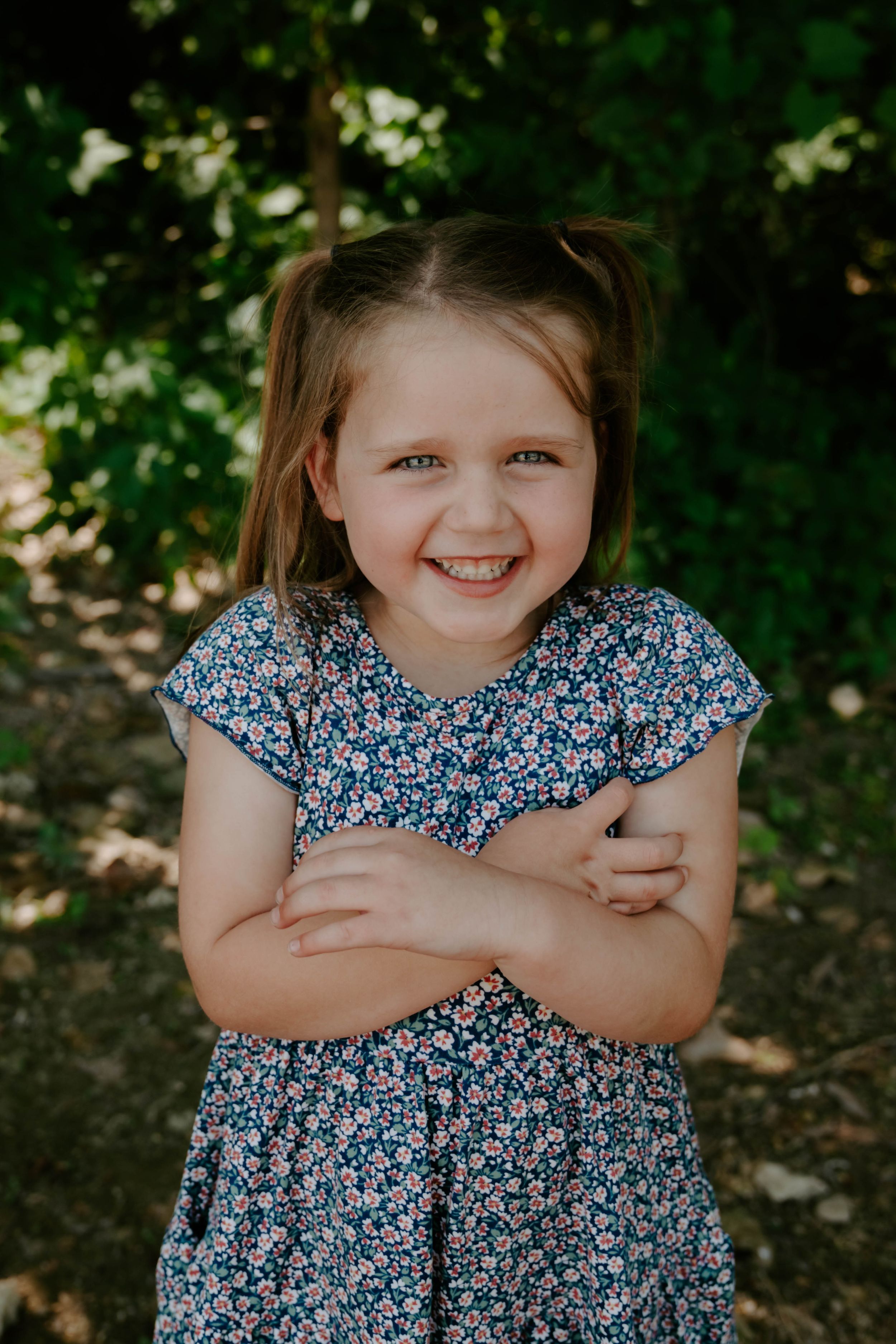 A joyful portrait of a child in a blue floral dress standing in dappled sunlight.