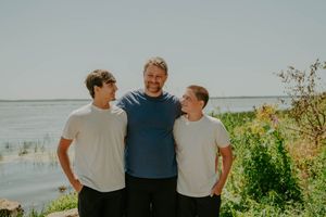 Casual family portrait taken outdoors with water and sky in the background.