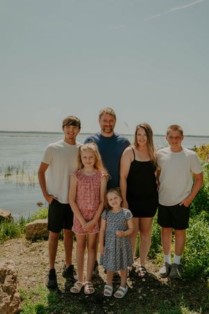 Family members pose together on a sunny day at the beach with water and vegetation in the background.