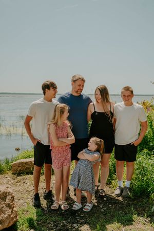 A casual group photo taken outdoors against a scenic waterfront backdrop on a bright summer day.