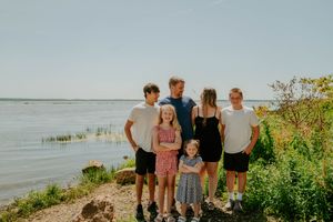 Group portrait captured on a natural shoreline with water and green foliage in the background.