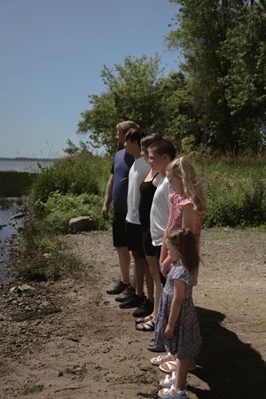 People lined up for a photo on a rocky beach path with water and trees visible in the distance.