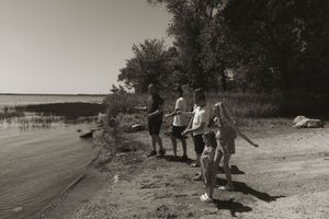 A black and white vintage photograph shows people walking along a shoreline on a sunny day.