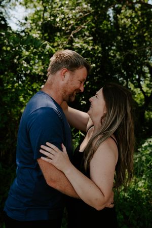 A romantic moment captured between two people embracing in a wooded outdoor setting.