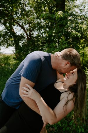 A romantic dip pose photographed in a lush green outdoor setting with natural lighting.