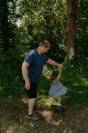A person bends down to examine something on a wooded trail on a sunny day.