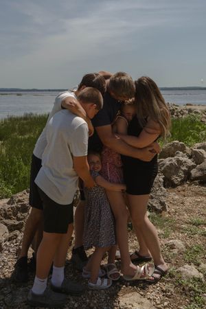 A group huddles together on a rocky coastal area near marsh grass.