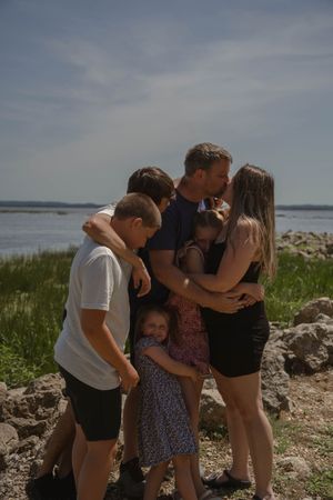 People share an intimate group moment on a rocky beach with water in the background.