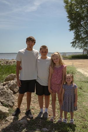 A group poses together on a grassy shoreline with water and trees in the background.