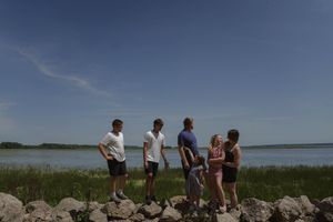 A group explores a rocky shoreline against a bright blue sky and water.