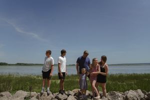 People gather on a rocky beach with marsh grass and water in the distance.