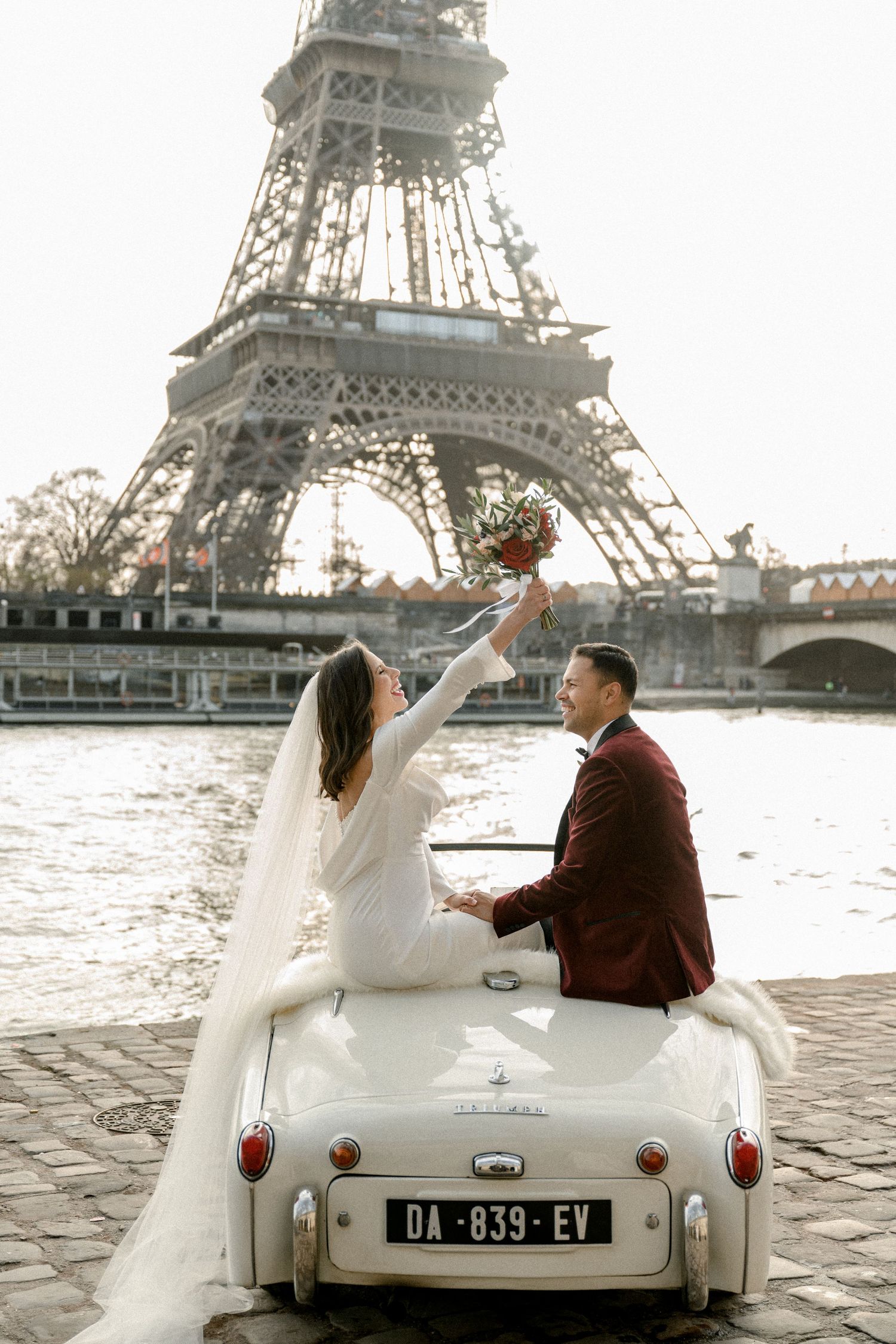 Romantic couple leaning against stone pillar near palm trees in Mediterranean architectural setting.