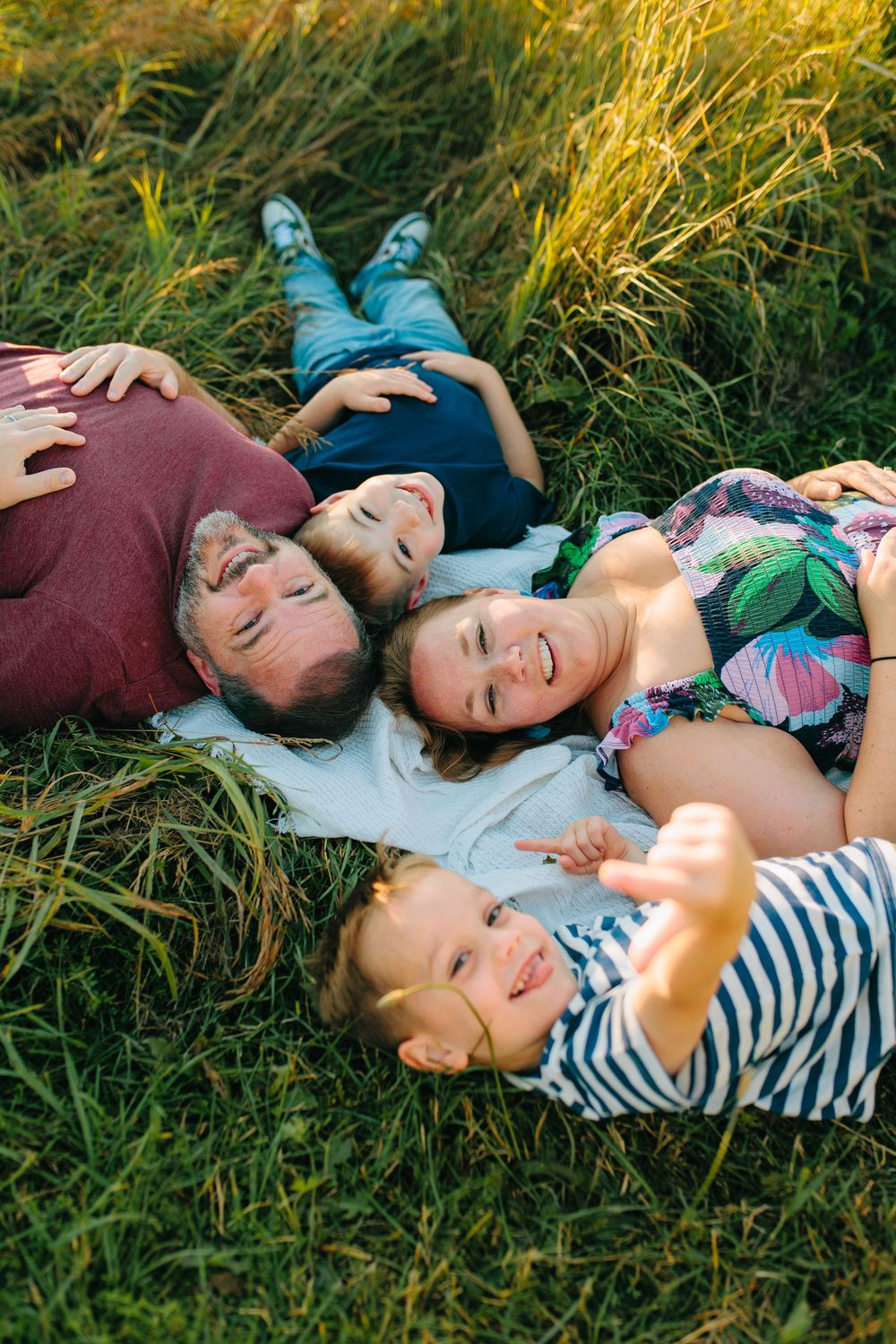 Group laying together in tall grass wearing casual clothes during sunset with golden light.