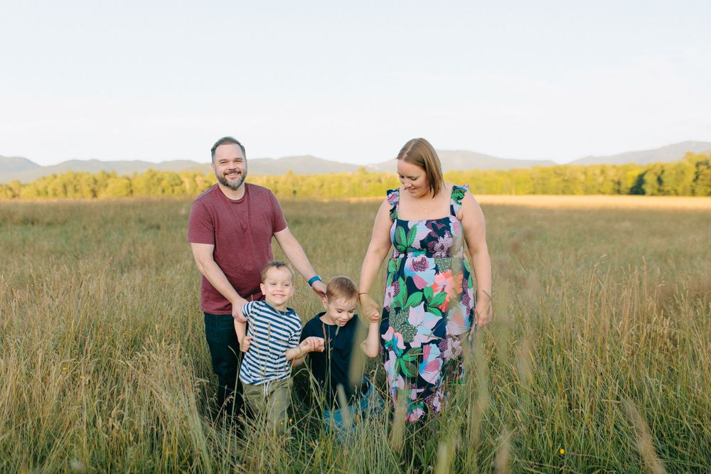 Family wearing coordinating outfits walks through tall grass in a golden field at sunset.