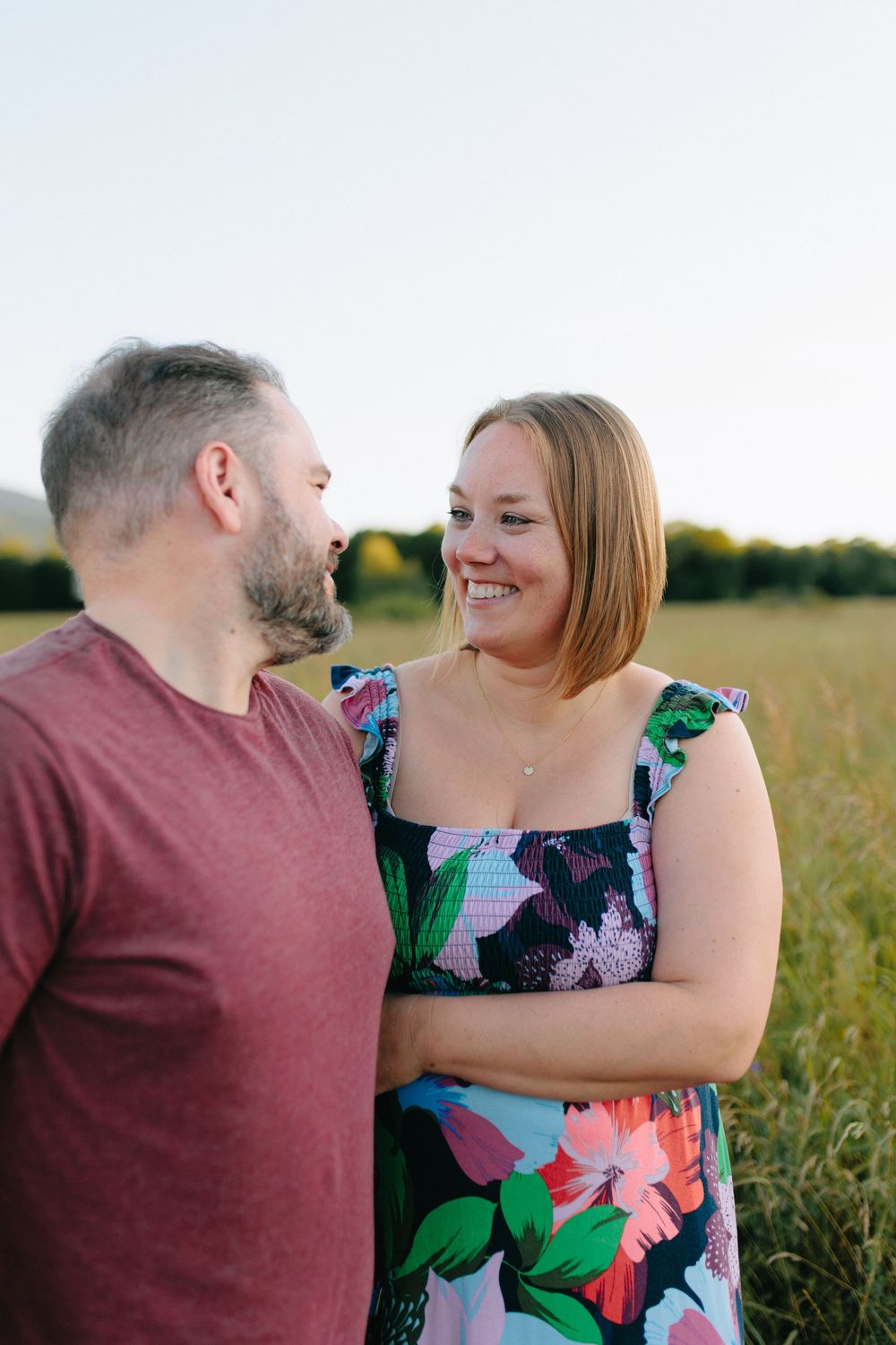 Couple sharing a tender moment together in a summer field at sunset wearing burgundy and floral print outfits.
