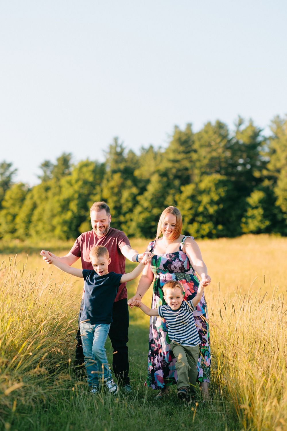 A family walks together through a sunlit golden meadow surrounded by green trees on a summer evening.