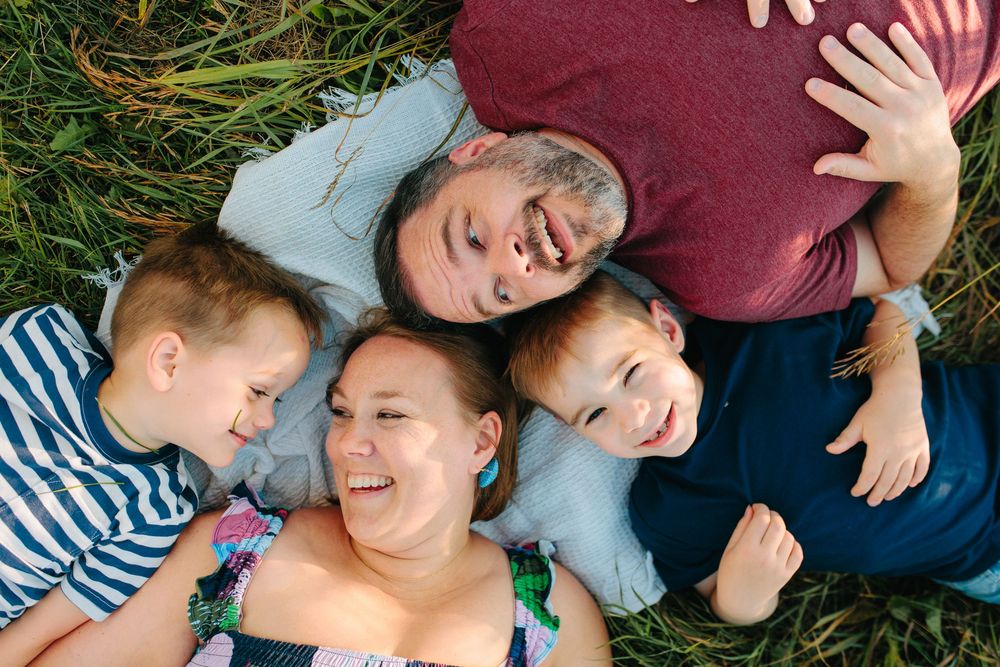 A group lies on a burgundy couch laughing and smiling together in casual attire during a relaxed gathering.