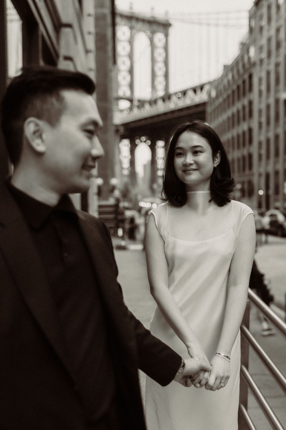 A romantic black and white photo of a couple posing near the Manhattan Bridge in DUMBO, Brooklyn.