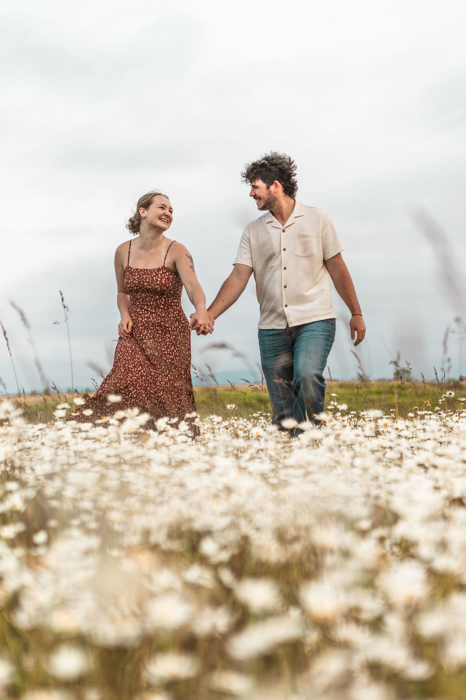 Couple walks hand in hand through a dreamy field of white wildflowers.
