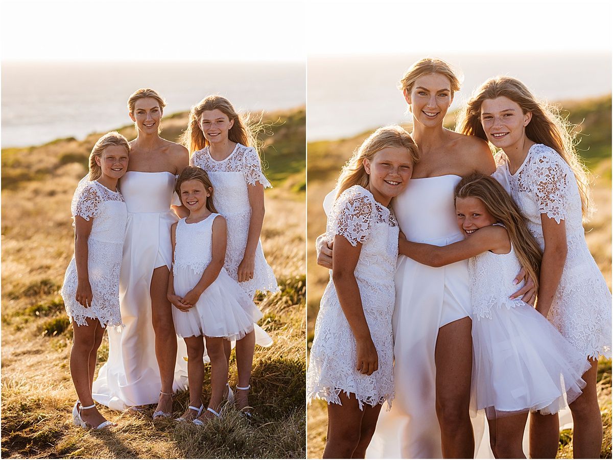 Family in coordinating white outfits poses together on grassy coastal hillside during golden hour.