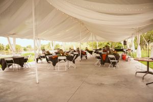 Interior of a large white wedding tent set up with round tables and chairs for an elegant reception celebration.