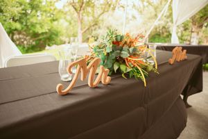 Elegant wedding reception table with dark tablecloth features wooden Mr sign and floral centerpiece on outdoor porch.