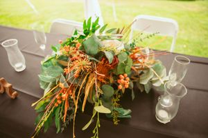 Floral centerpiece arrangements with greenery and orange blooms decorate a dark wooden dining table.