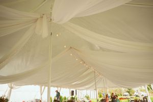 White fabric drapes elegantly across the ceiling of an outdoor event tent creating an ethereal canopy effect.