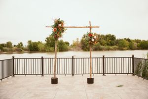 Wooden wedding arch decorated with autumn flowers stands on stone patio overlooking a serene lake.