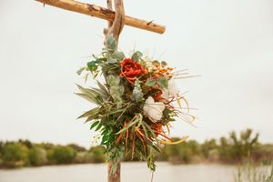 Beautiful floral arrangement with red and white blooms adorns a wooden cross against a waterfront landscape.
