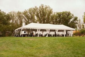 White wedding tent set up on a green lawn with tables and chairs arranged underneath for an outdoor reception event.